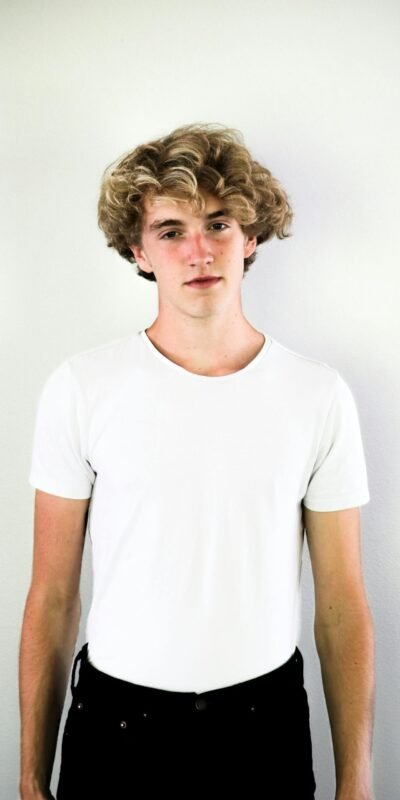 Portrait of a teenage boy with curly hair in a white shirt, standing against a white background.