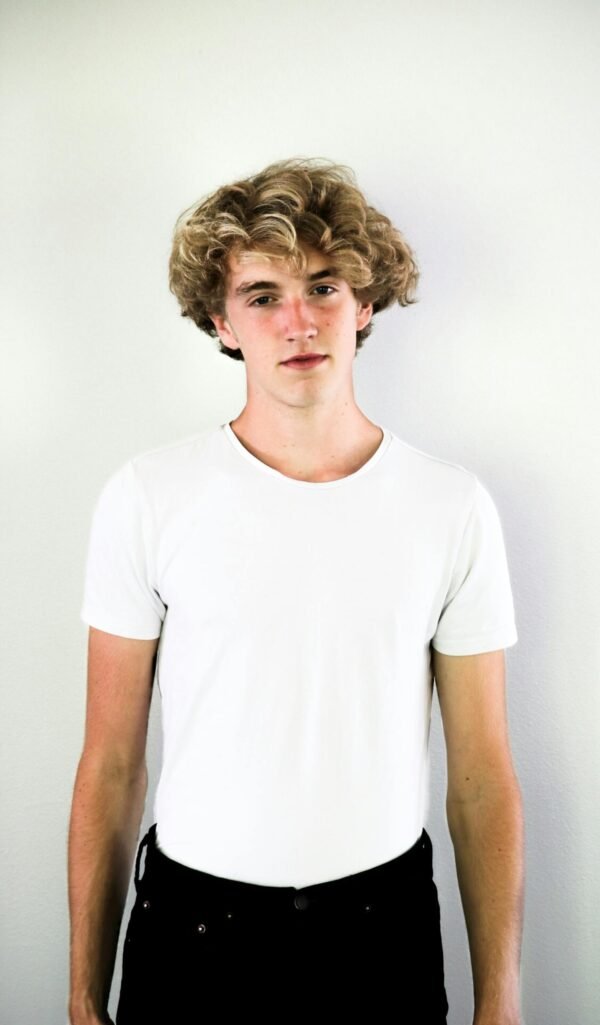 Portrait of a teenage boy with curly hair in a white shirt, standing against a white background.